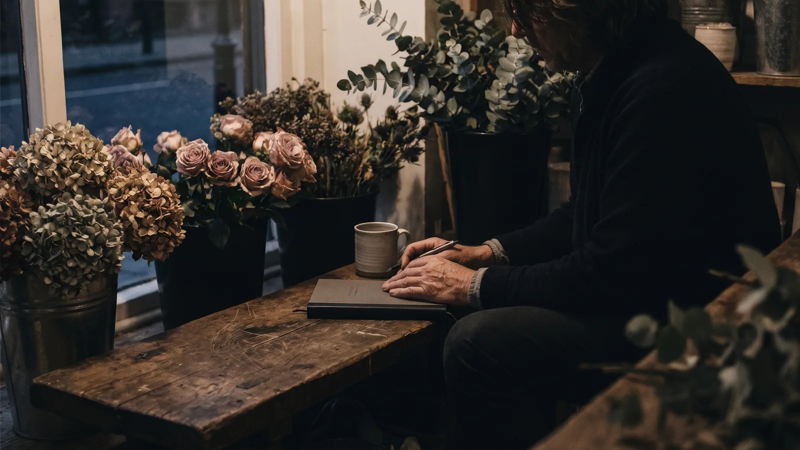 A florist at a workbench among buckets of flowers at the end of the day, planning which jobs to hand off